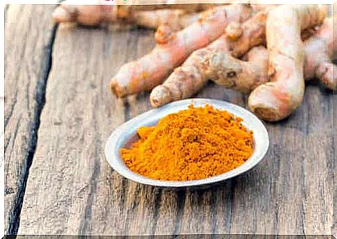 Ground turmeric on a wooden table with turmeric root behind it