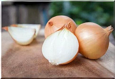 Whole and cut onions on a wooden cutting board