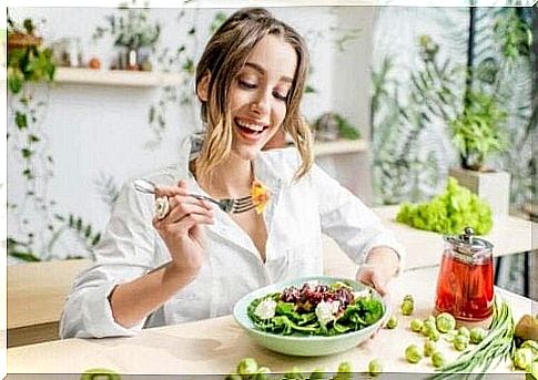 A woman smiles and eats a salad